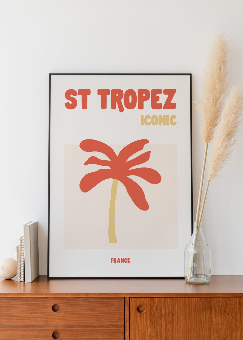 Affiche déco Saint-Tropez Iconic avec palmier rouge et tronc ocre sur fond blanc, encadrée sur meuble en bois.